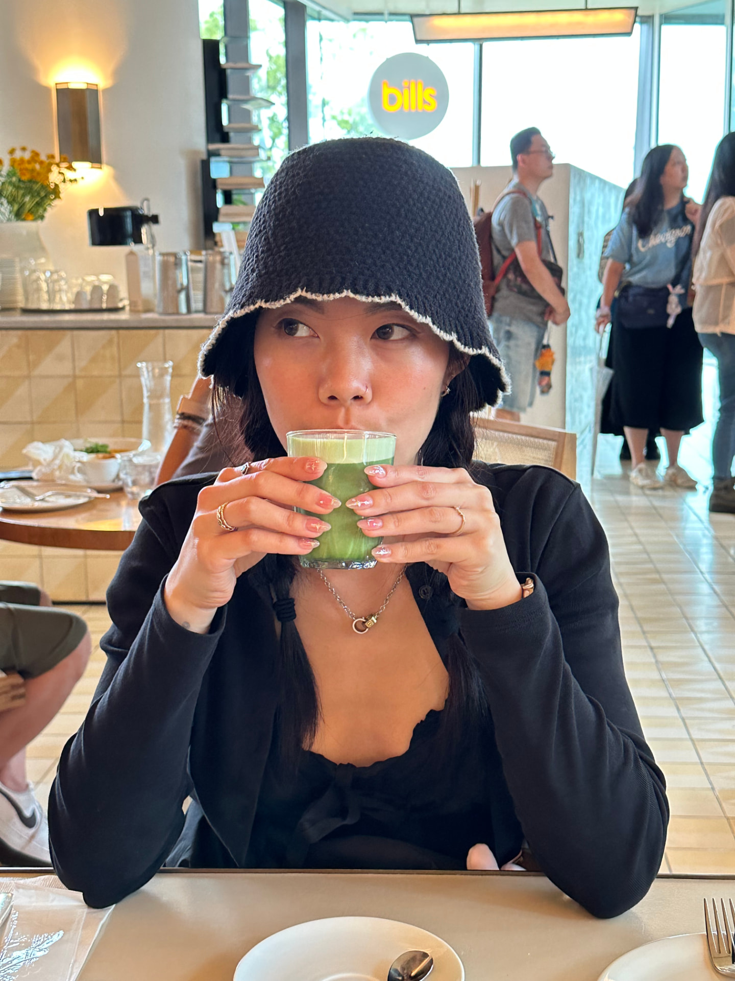 Esther sipping a glass of matcha at a cafe table